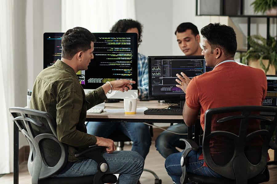 四个人坐在电脑前，一边讨论一边指着屏幕上的文字